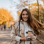 a woman smiling in a park while holding a cup of coffee