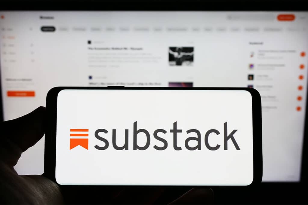 Person holding cellphone with logo of subscription company Substack on screen in front of business webpage