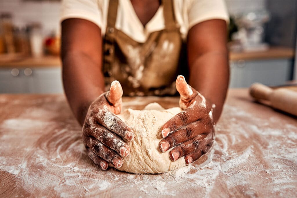 Close up of black female hands molding raw dough on wooden table powdered with flour