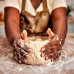 Close up of black female hands molding raw dough on wooden table powdered with flour