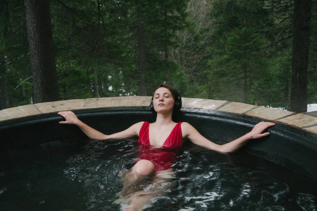 Woman listening to Myndstream on headphones in a hot tub in the woods