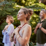 Group of people standing outdoors with hands on their hearts, practicing mindfulness in a wellness retreat